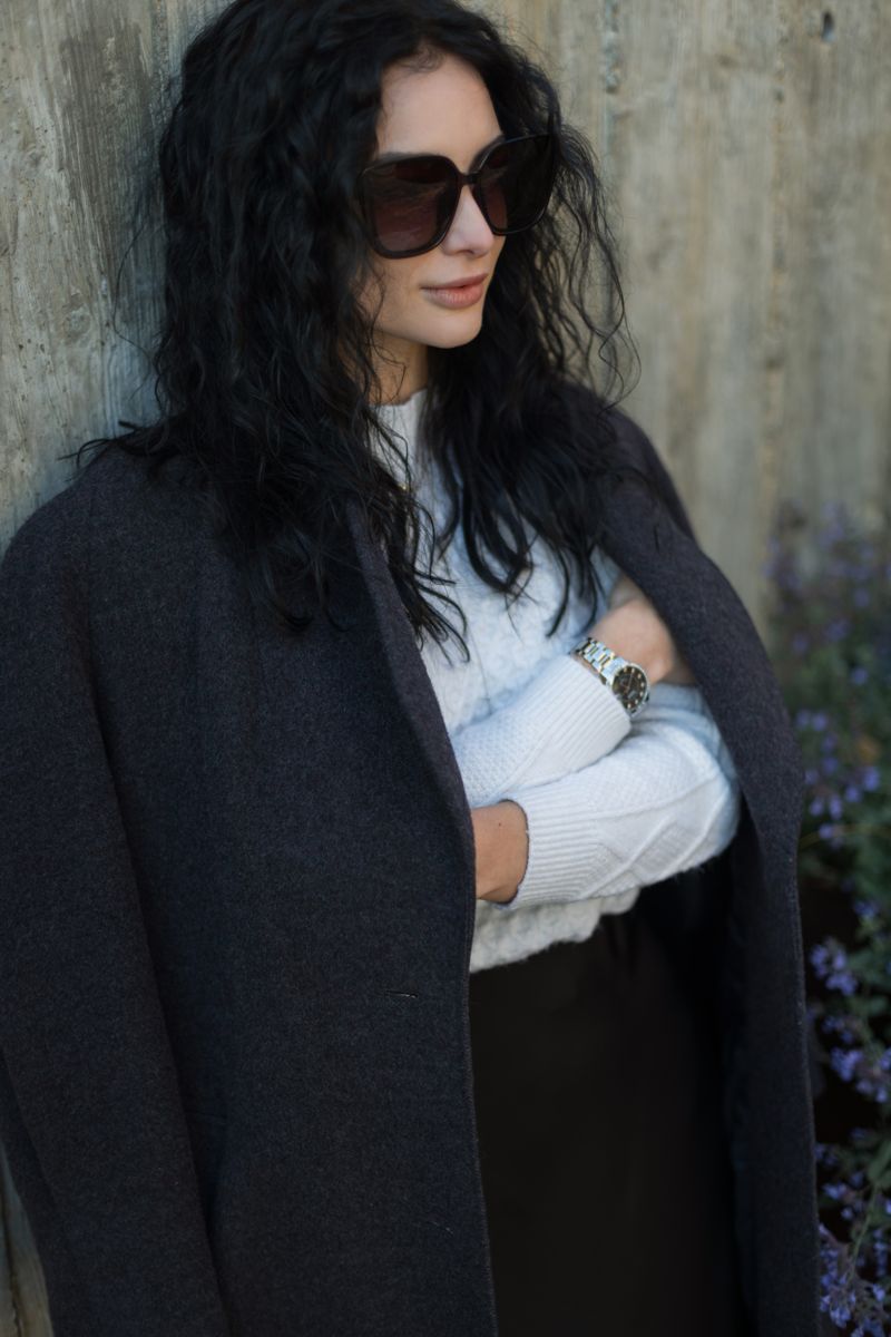 Woman with a dark coat draped over her shoulders and oversized sunglasses