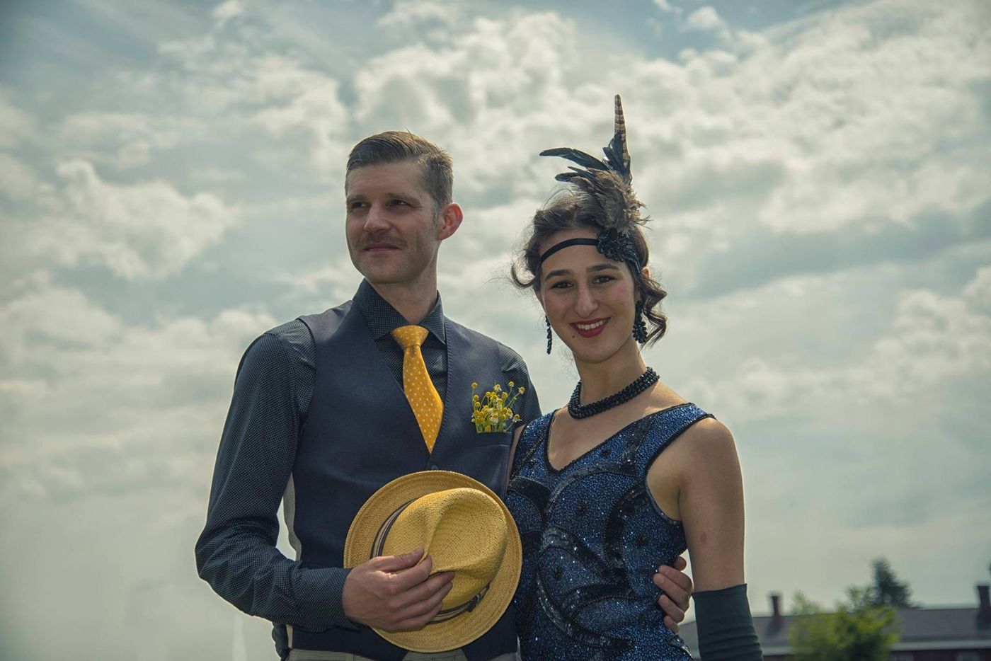 Couple in 1920s vintage dress — straw boater and feathered headpiece — against a summer sky
