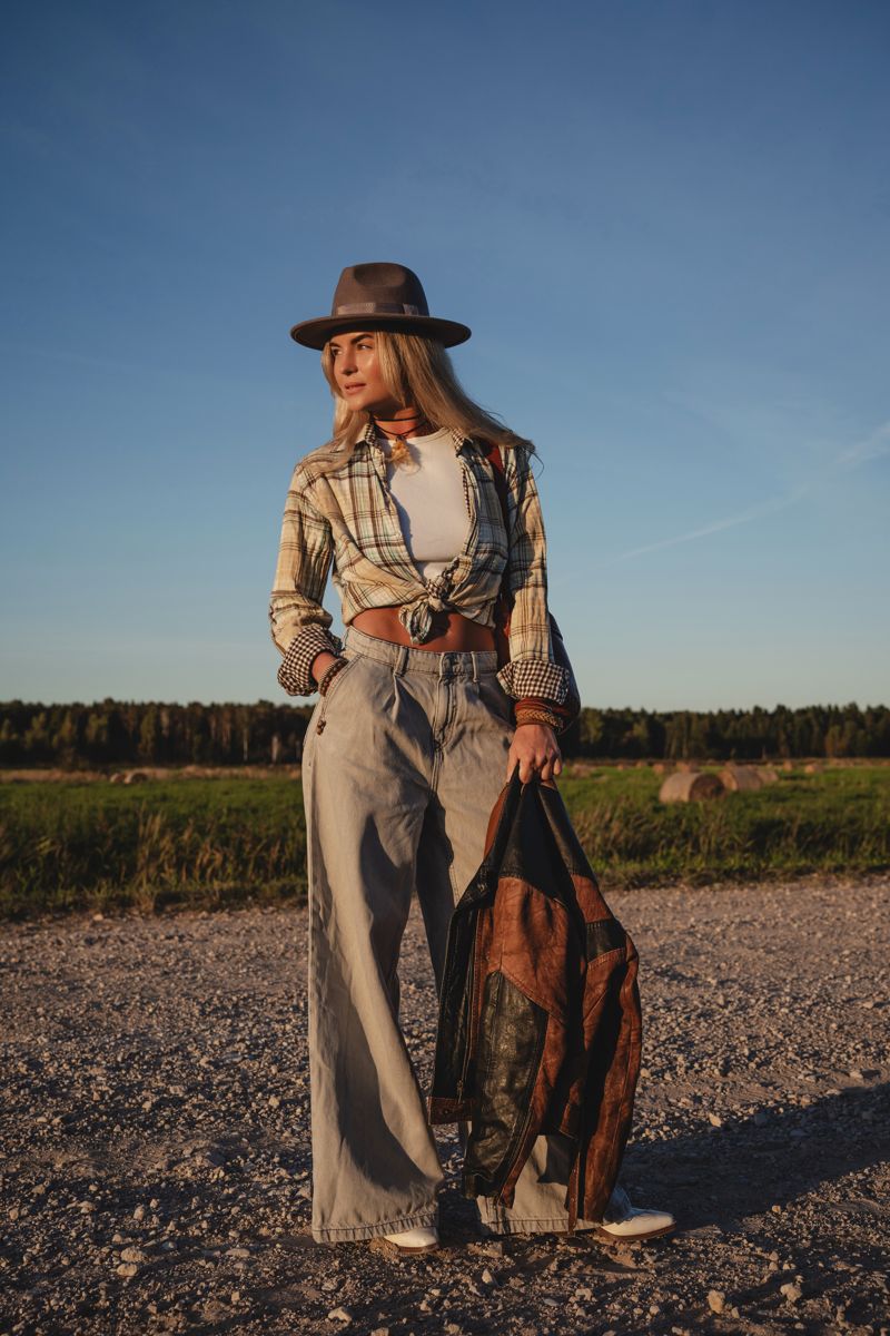 Woman in plaid, hat and denim on a gravel road at golden hour
